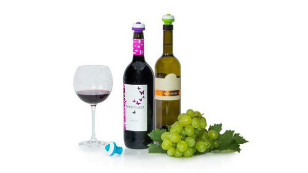 Steklenici vina z vakuumskimi zamaški, natočen kozarec črnine in grozdje na belem ozadju.